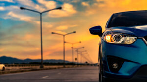 Blaues Kompakt-SUV-Auto mit offenem Scheinwerferlicht, das bei Sonnenuntergang mit schönem Himmel und Wolken auf einer Betonstraße in der Nähe des Berges geparkt wurde.