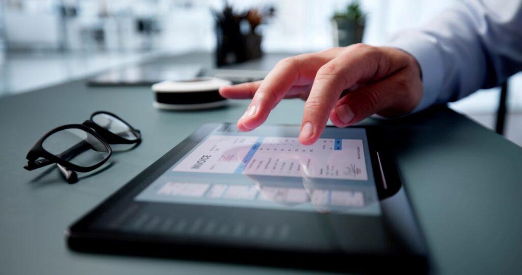 Hand nutzt Tablet zur digitalen Rechnungserfassung mit Spesen App am Schreibtisch