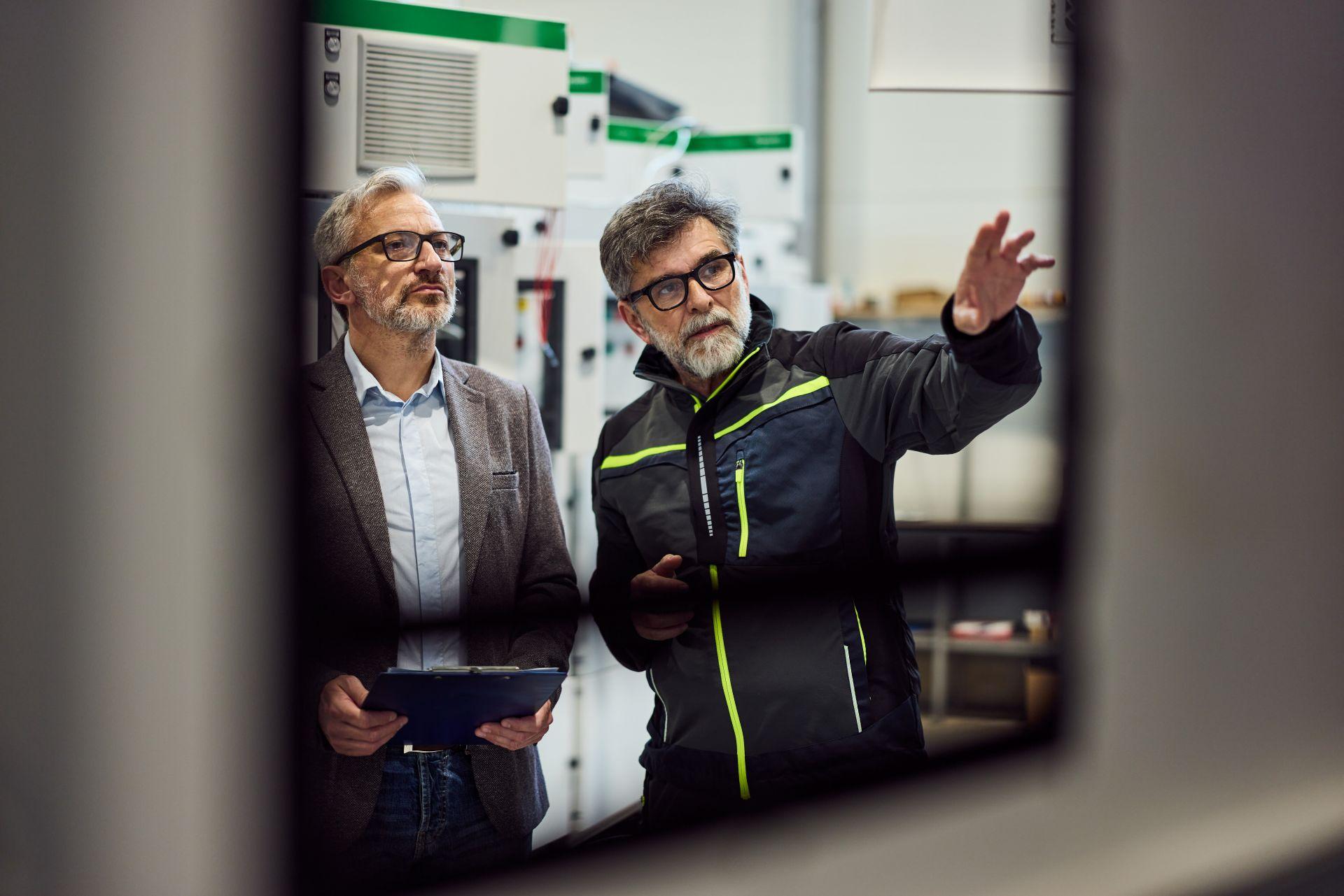 Zwei Männer im technischen Fachgespräch vor Maschine – symbolisiert strategische Planung und Bewertung im Produktionsumfeld