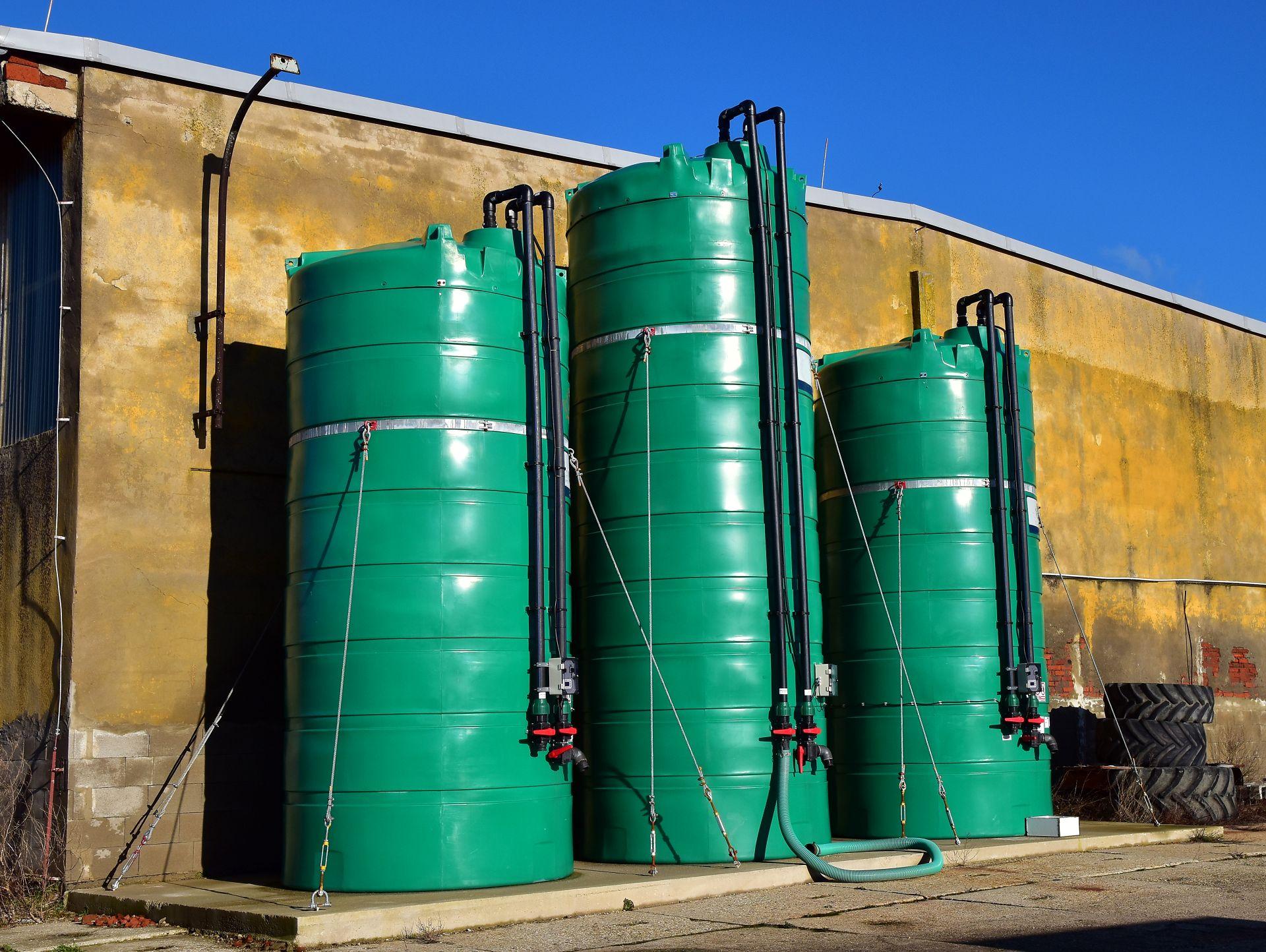 Drei gruene Fluessigduengertanks vor landwirtschaftlicher Halle unter blauem Himmel, zeigen sichere Lagerung von Fluessigduenger