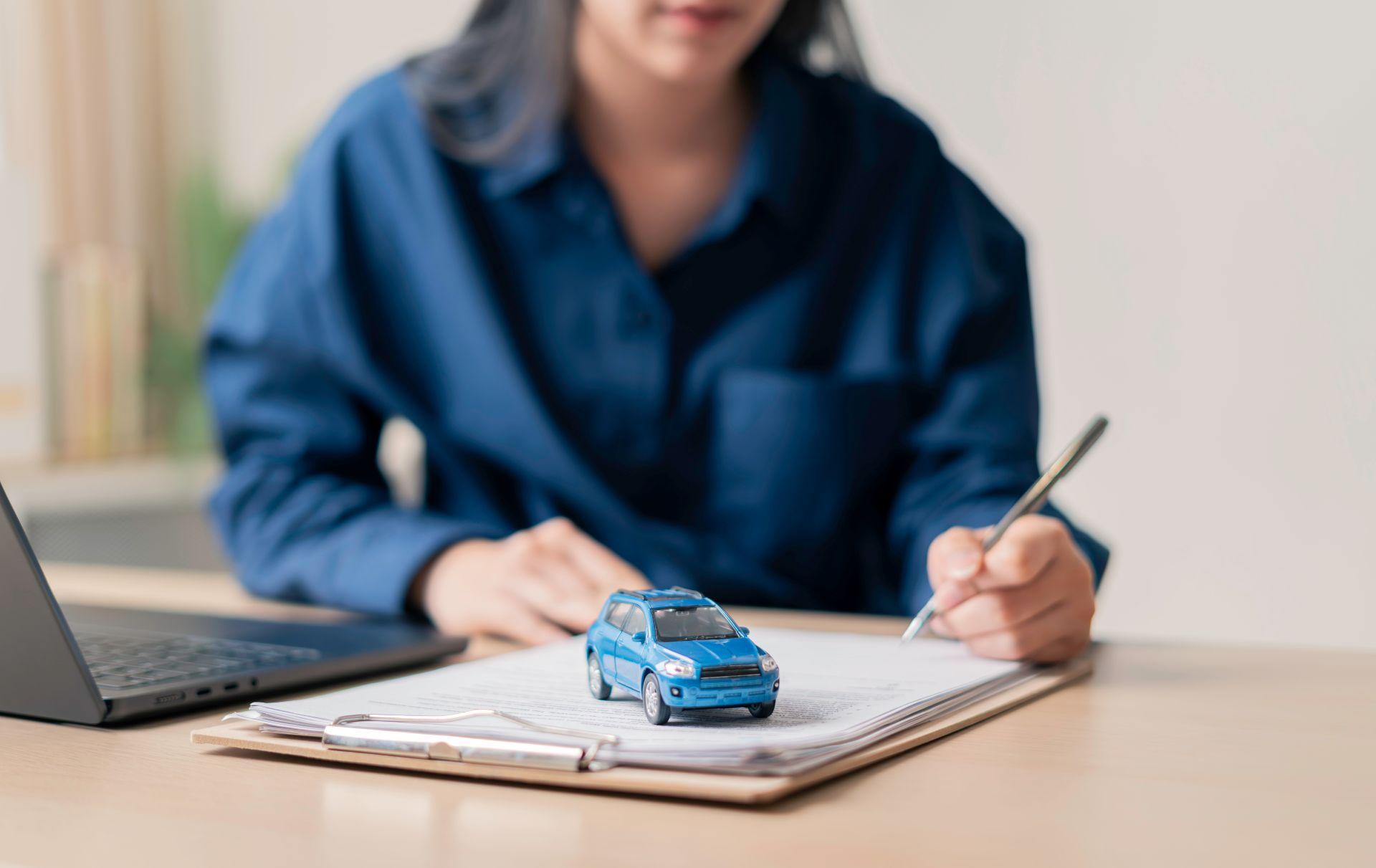 Frau unterschreibt Zulassungsunterlagen, Spielzeugauto liegt als Symbol auf dem Formular